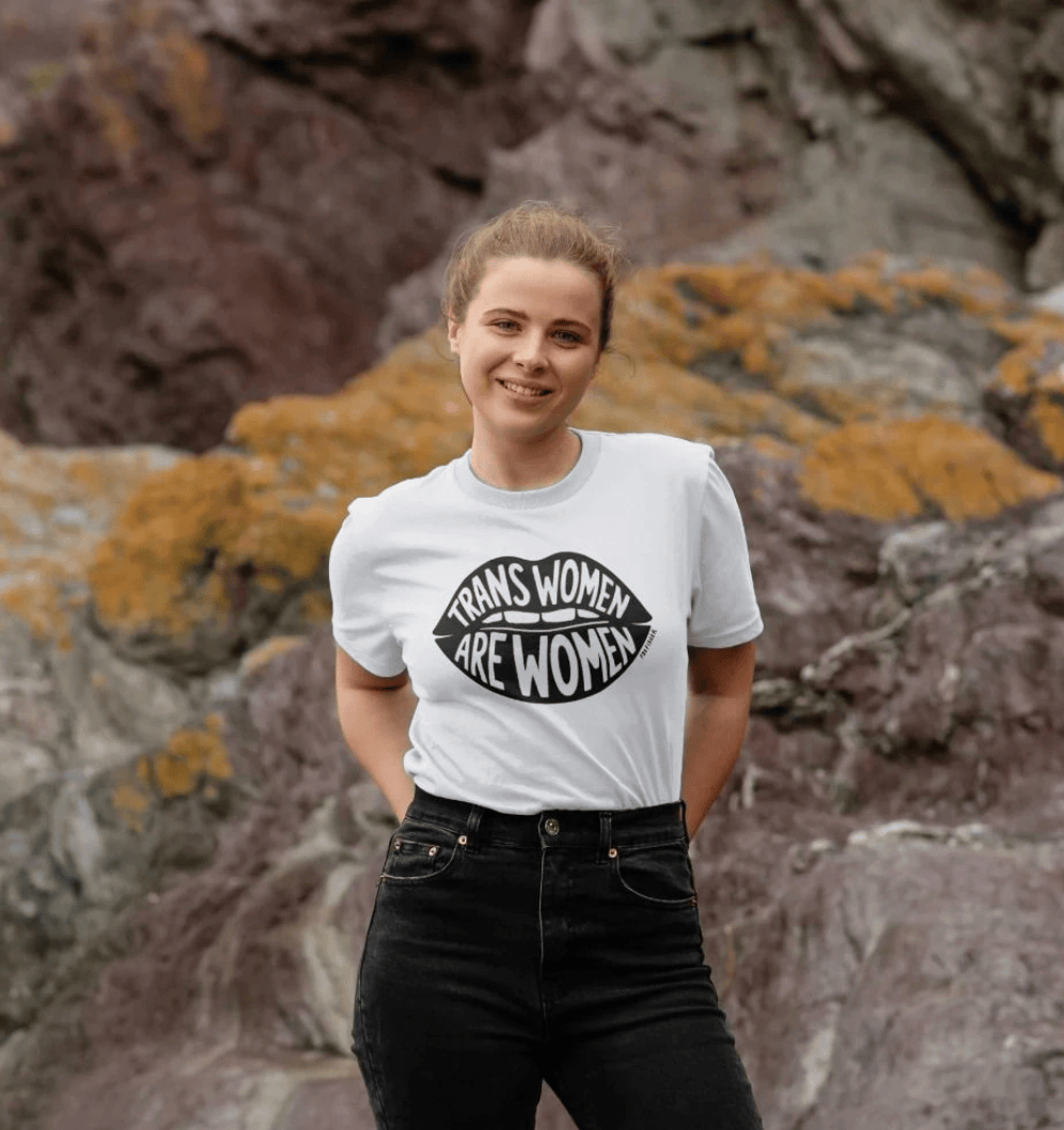 Model wearing white Trans Women Are Women t-shirt outdoors by Fox Fisher, organic cotton feminist graphic tee in natural setting