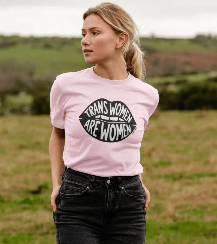 Model wearing pink Trans Women Are Women t-shirt in a green field by Fox Fisher, organic cotton feminist graphic tee lifestyle photo