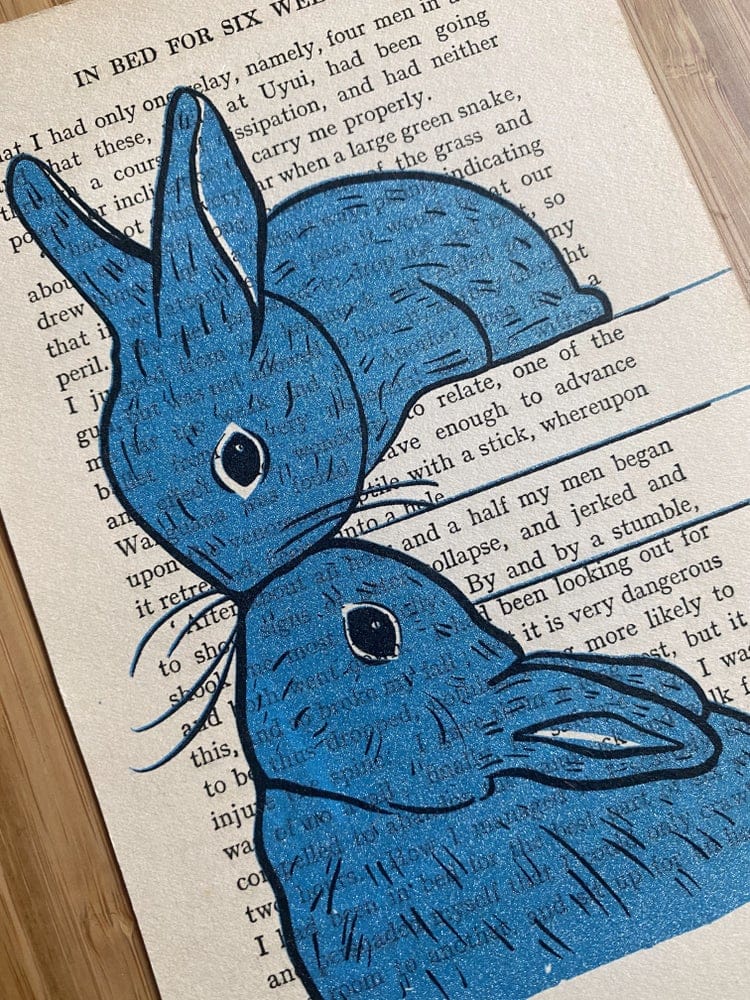 Two blue rabbits screen print by Fox Fisher on vintage book page, hand-pulled ink illustration from Fox's Snail Mail Art Club subscription