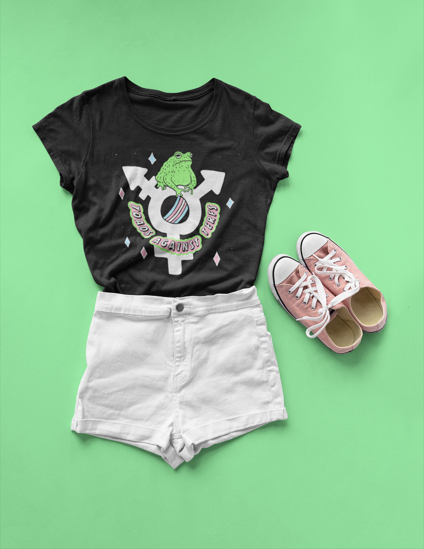 A t shirt from a trans rights and LGBTQIA+ collection created by Fox Fisher. This image features a toad and the trans symbol with text Toads Against TERFs