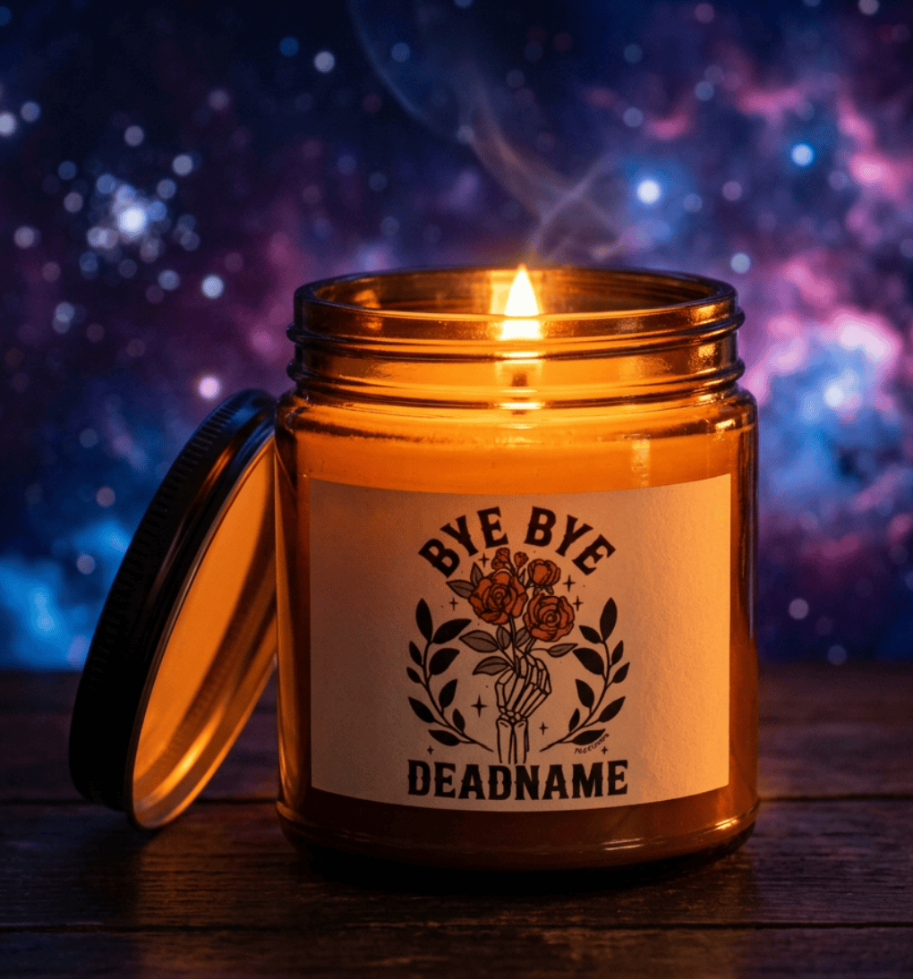 Bye Bye Deadname soy wax candle lit on wooden surface, hand-poured candle in amber jar with Fox Fisher skeleton rose label, galaxy background