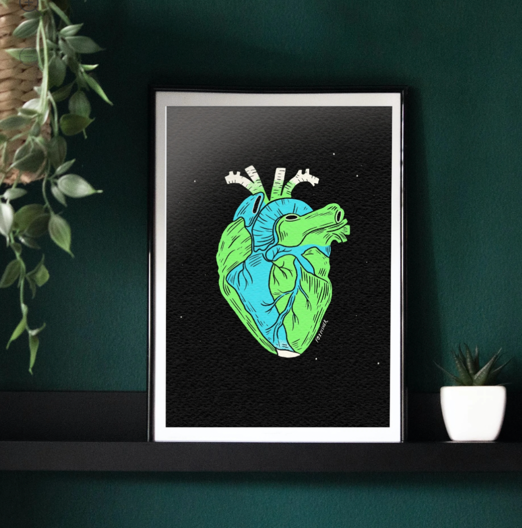 Earth Is A Heart Art Print by Fox Fisher - Anatomical heart illustration in green and blue earth tones, framed on a dark wall with plants, A3 eco-friendly recycled paper print
